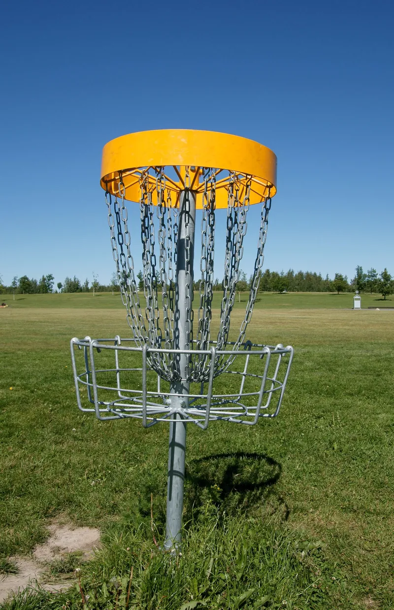 A disc golf basket with a yellow band standing on open, mown grass on a sunny summer day