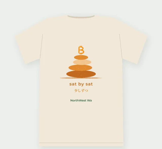 Natural tee, back view: a stacked-stone cairn in warm orange with “sat by sat” and 少しずつ underneath