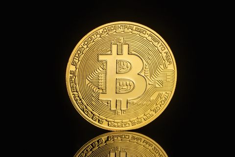 Gold Bitcoin coin standing on a black reflective surface